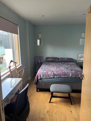Een slaapkamer met een bed, een bureau, een stoel en een bankje.
