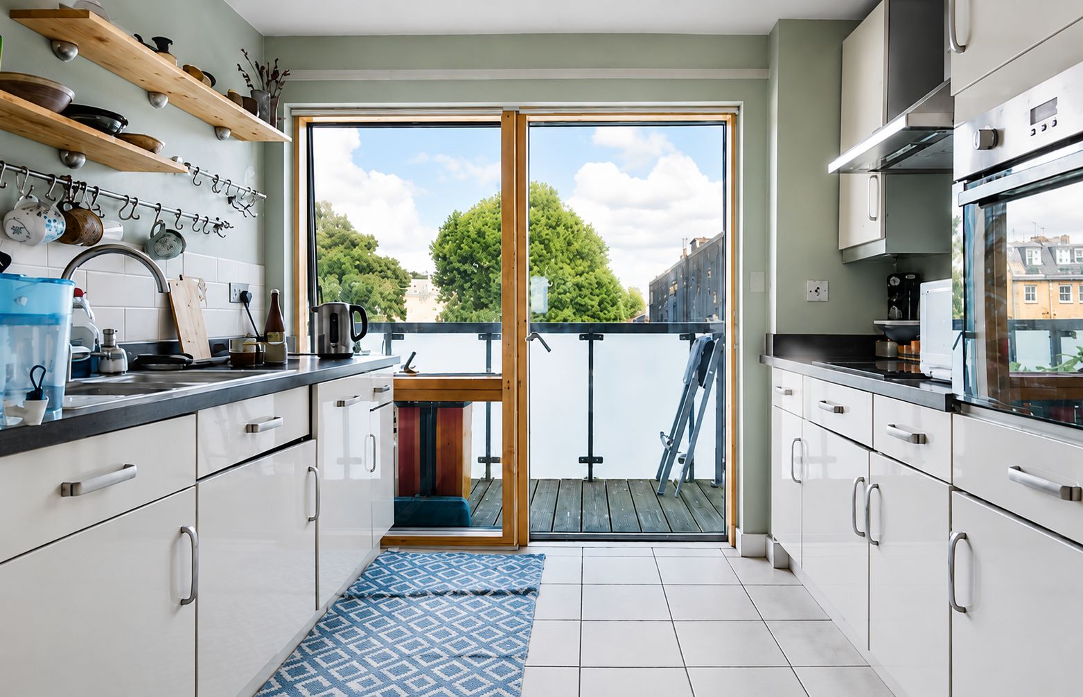 A modern kitchen with white cabinets, a black countertop, and a view of a river through a glass door.