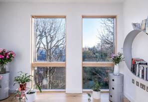 Ein modernes Zimmer mit großen Fenstern, einem Bücherregal und Topfpflanzen.