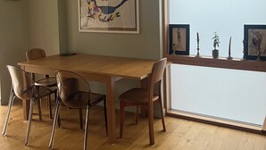 A dining area with a wooden table and chairs, a large window, and a framed artwork on the wall. - 2 bedroom 2 bathroom apartment in West Hampstead/ Finchley Road London (London)