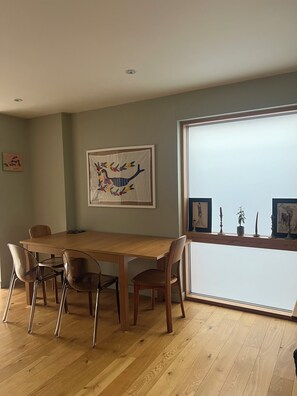 Een eetruimte met een houten tafel en stoelen, een groot raam en een kunstwerk in een lijst aan de muur.