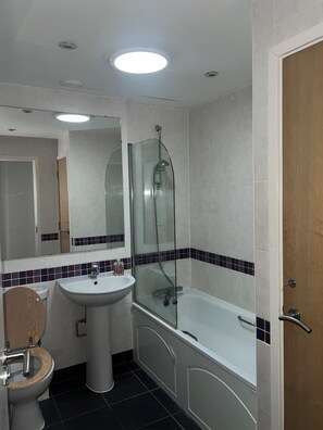 Een moderne badkamer met een douchecabine van glas, een witte wastafel en een houten toilet.