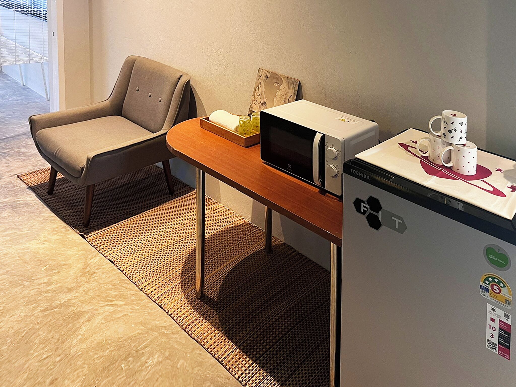 A small kitchenette with a microwave, refrigerator, and a chair.