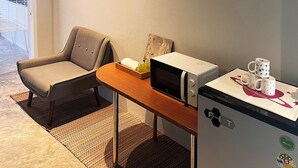 Uma pequena cozinha compacta com micro-ondas, geladeira e uma cadeira.