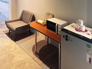 A small kitchenette with a microwave, refrigerator, and a chair. - Human Touch Rooms (Krung Thep Maha Nakhon)