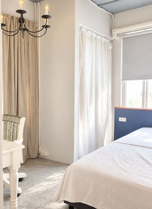 A bedroom with a bed, a chair, a window with a blind, and a chandelier.