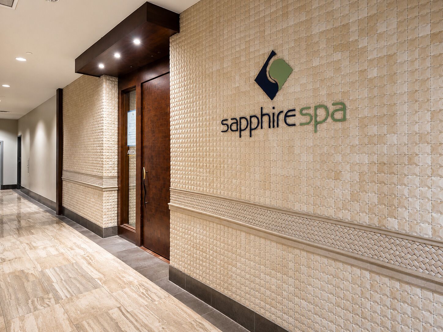 Un couloir avec un mur à texture et une porte portant l’inscription « spa Saphir ».