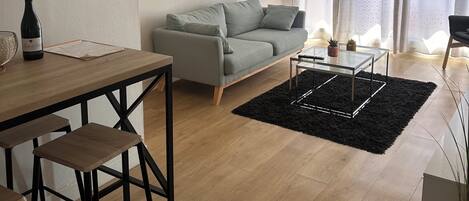 A modern living room with a grey sofa, a glass coffee table, and a black rug.