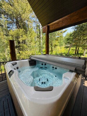 A hot tub on a wooden deck with a view of trees. - Deer Creek Lodge -12 min. to YNP+Hot tub+AC+Sauna Sleeps 26 (Island Park)