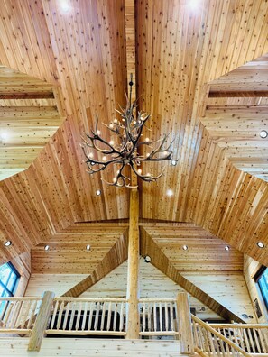 A wooden interior with a central chandelier, wooden beams, and a staircase.