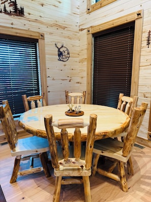A wooden interior with a round table surrounded by chairs with wooden legs. - Deer Creek Lodge -12 min. to YNP+Hot tub+AC+Sauna Sleeps 26 + New Built 2026 (Island Park)