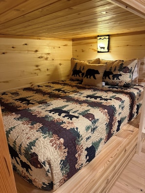 A wooden cabin bedroom with a bed, two pillows with bear designs, and a wall-mounted light. - Deer Creek Lodge -12 min. to YNP+Hot tub+AC+Sauna Sleeps 26 + New Built 2026 (Island Park)