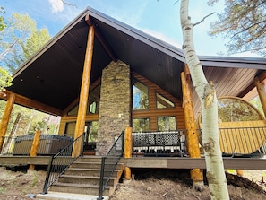 A cabin with a stone chimney, wooden beams, and a covered porch. - Deer Creek Lodge -12 min. to YNP+Hot tub+AC+Sauna Sleeps 26 (Island Park)