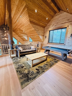A cozy cabin interior with a wooden ceiling, a sofa, a coffee table, a pool table, and a stone fireplace. - Deer Creek Lodge -12 min. to YNP+Hot tub+AC+Sauna Sleeps 26 + New Built 2026 (Island Park)