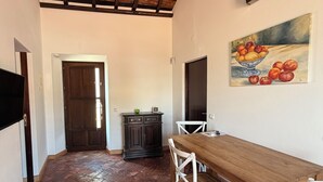Un comedor con una mesa de madera y sillas blancas, piso de baldosas, un armario de madera oscura y un cuadro en la pared.