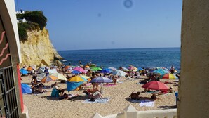 A beach with people sunbathing and umbrellas, a clear sky, and a view of the sea.