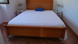 Una cama individual estándar con cabecera de madera, dos mesitas de noche con lámparas y suelo de baldosas.