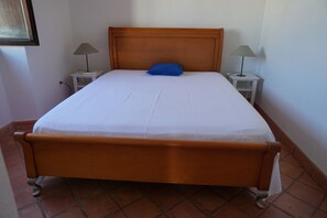 Un lit simple standard avec une tête de lit en bois, deux tables de chevet avec des lampes et un sol carrelé.