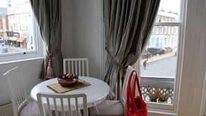 A room with a round table, white chairs, a bowl of fruit, and a red bag. - Mezzanine studio flat in the heart of Notting Hill (London)