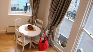 A cozy living room with a sofa, a dining table with chairs, a red bag, and large windows with curtains. - Mezzanine studio flat in the heart of Notting Hill (London)