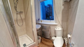 A bathroom with a shower, toilet, sink, and a window with a view of buildings. - Mezzanine studio flat in the heart of Notting Hill (London)