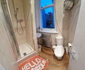 A bathroom with a shower, toilet, sink, and a window with a view of buildings. - Mezzanine studio flat in the heart of Notting Hill (London)