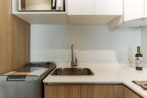 A kitchen with a stainless steel sink, a washing machine, and a wine bottle on the counter. - Hestia Stays at Fitz Roy 1900 (Buenos Aires)