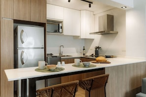 A modern kitchen with a built-in refrigerator, microwave, and stove. There are two bar stools and a small dining table. - Hestia Stays at Fitz Roy 1900 (Buenos Aires)