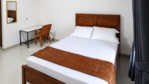 A hotel room with a wooden ceiling, a bed with white bedding, a desk with a chair, and an air conditioning unit. - Waetuak Homestay (Manggarai barat)