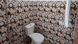 A bathroom with a toilet, shower, and a patterned wall. - Waetuak Homestay (Manggarai barat)