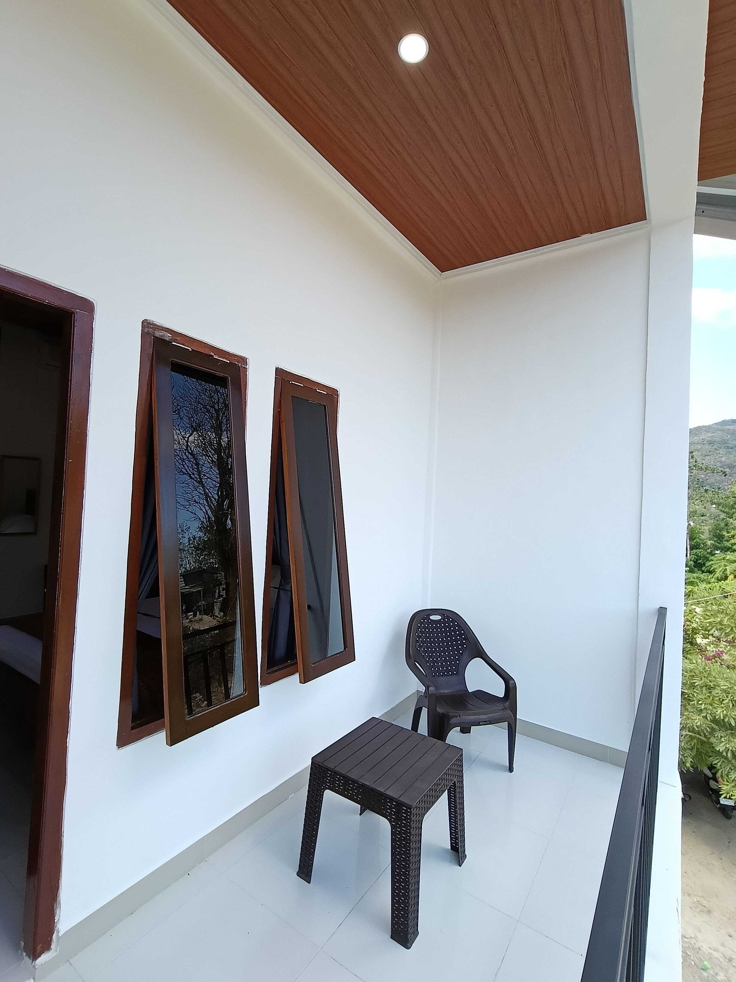 A balcony with a wooden ceiling, white walls, and a small table with a chair.