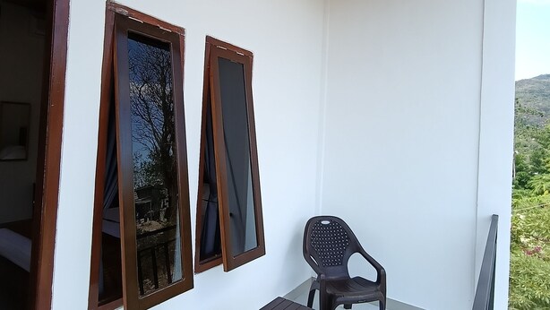 A balcony with a wooden ceiling, white walls, and a small table with a chair. - Waetuak Homestay  (Labuan Bajo)