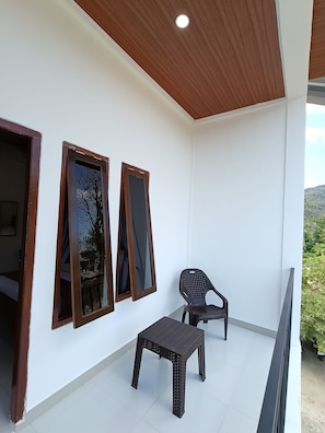 Un balcón con techo de madera, paredes blancas y una pequeña mesa con una silla.