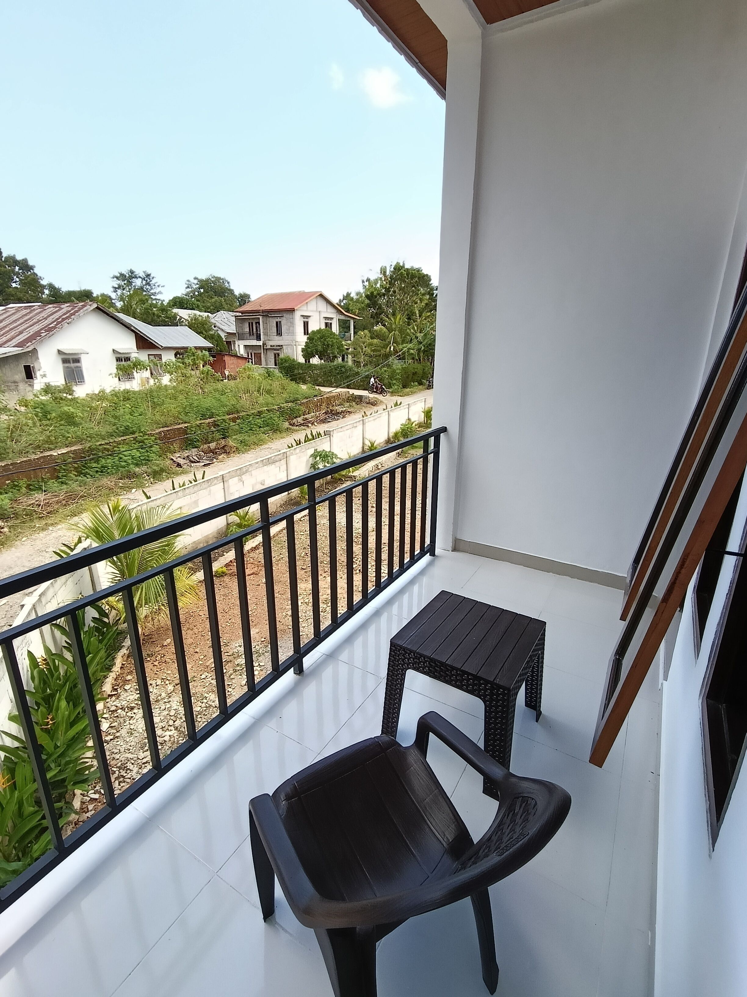 Un balcón con una silla negra, una mesita y vistas a casas y follaje.