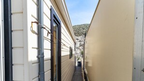 Un estrecho pasillo con piso de madera, pared color beige y ventana con marco negro.