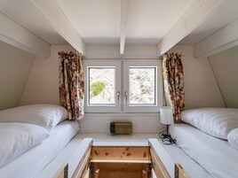 Una habitación pequeña y triangular con dos camas, una ventana y un calentador.