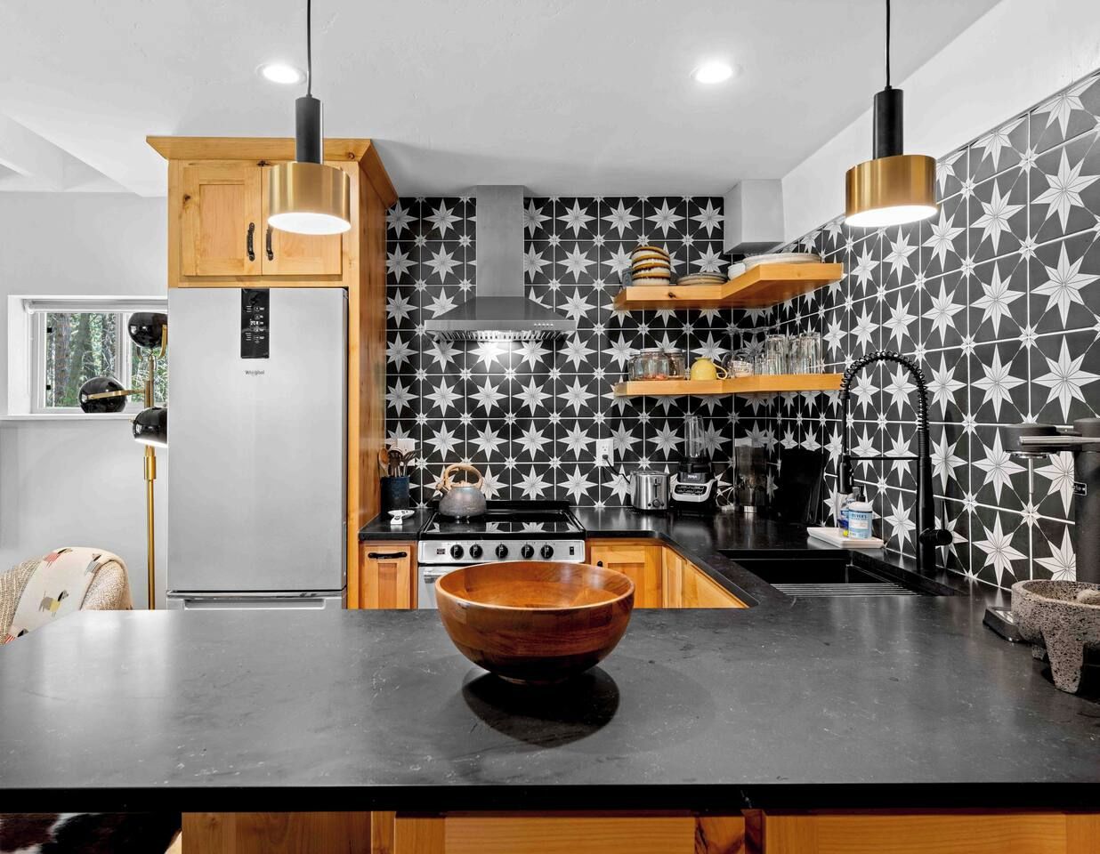 Una cocina moderna con una isla grande, armarios de madera, un refrigerador de acero inoxidable y un salpicadero con diseño.