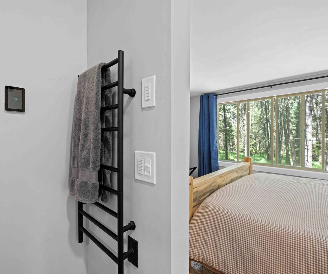 A bedroom with a bed, a towel rack, a thermostat, and a window with a view of trees.
