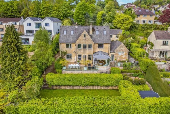 Et stort hus med en velplejet have, et spejløb og en pavillon.