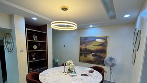 A dining area with a round table, chairs, a ceiling light, a fan, and a painting on the wall. - Spacious 4-bedroom townhome in peaceful Lagos with AC, pool and gym (Lagos)
