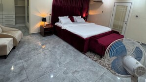 A hotel room with a bed, a bedside table, a lamp, a fan, and a wardrobe. - Spacious 4-bedroom townhome in peaceful Lagos with AC, pool and gym (Lagos)