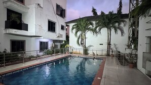 A swimming pool with a tiled deck, surrounded by a building with multiple balconies and palm trees. - Spacious 4-bedroom townhome in peaceful Lagos with AC, pool and gym (Lagos)