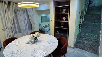 A dining area with a round table, brown chairs, a white fan, and a staircase with a green-lit railing.