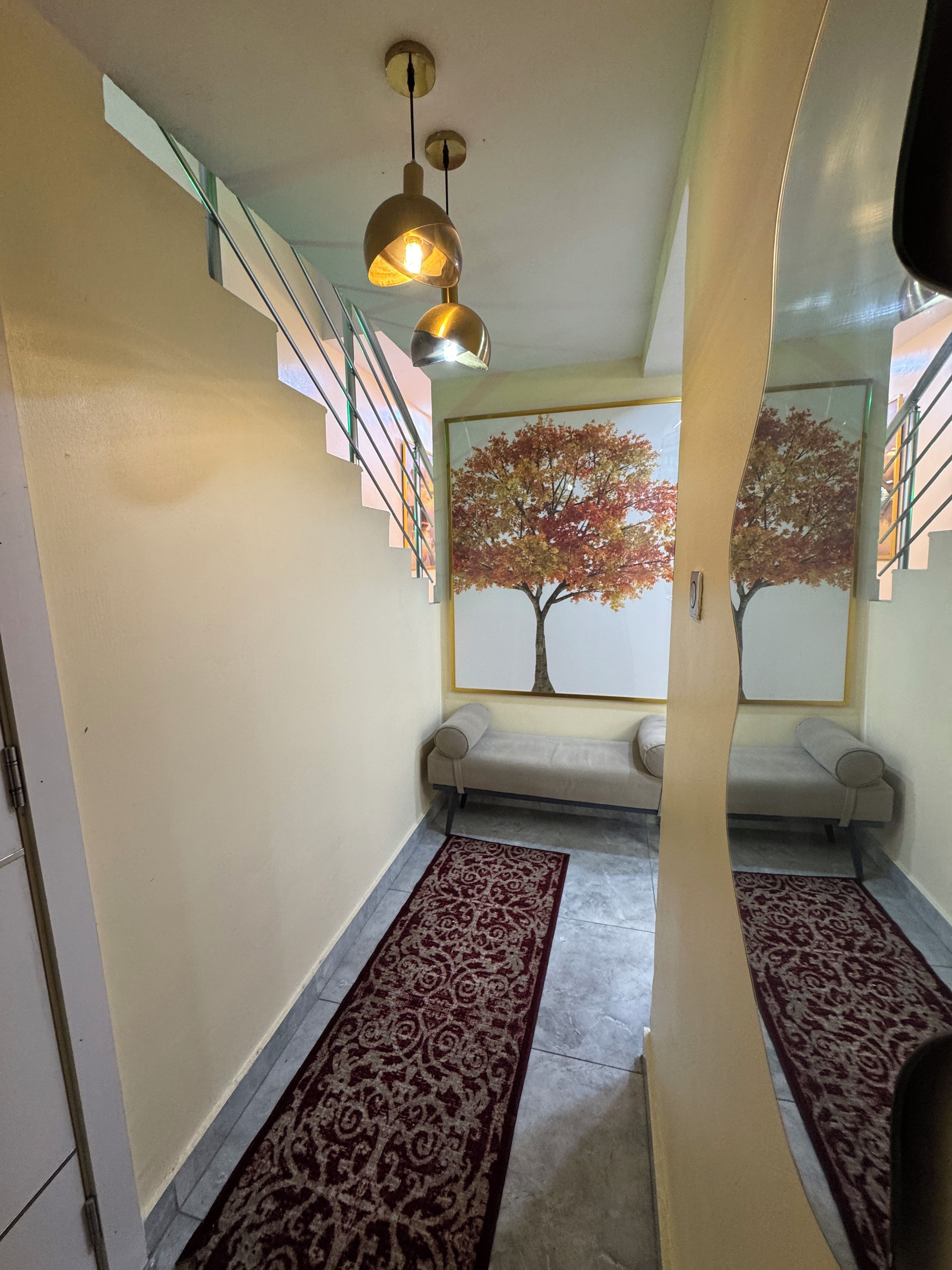 A hallway with a staircase, a bench, and a patterned rug.
