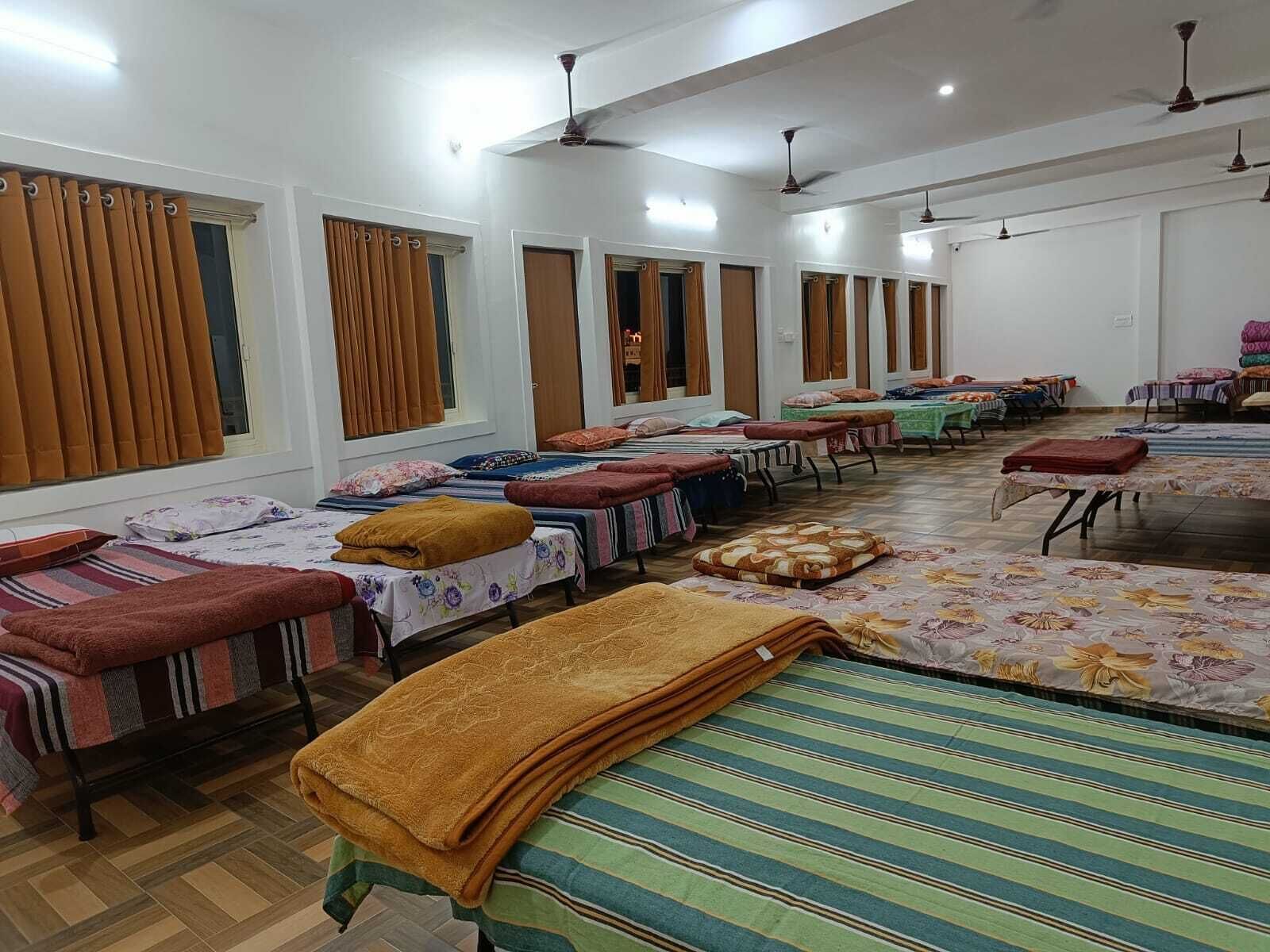 Habitación de hotel con varias camas, cada una con una manta de color diferente, y una cama grande con una manta a rayas.