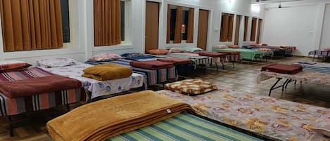 Una habitación de hotel con varias camas, cada una con un edredón de color diferente, y un ventanal grande con cortinas.
