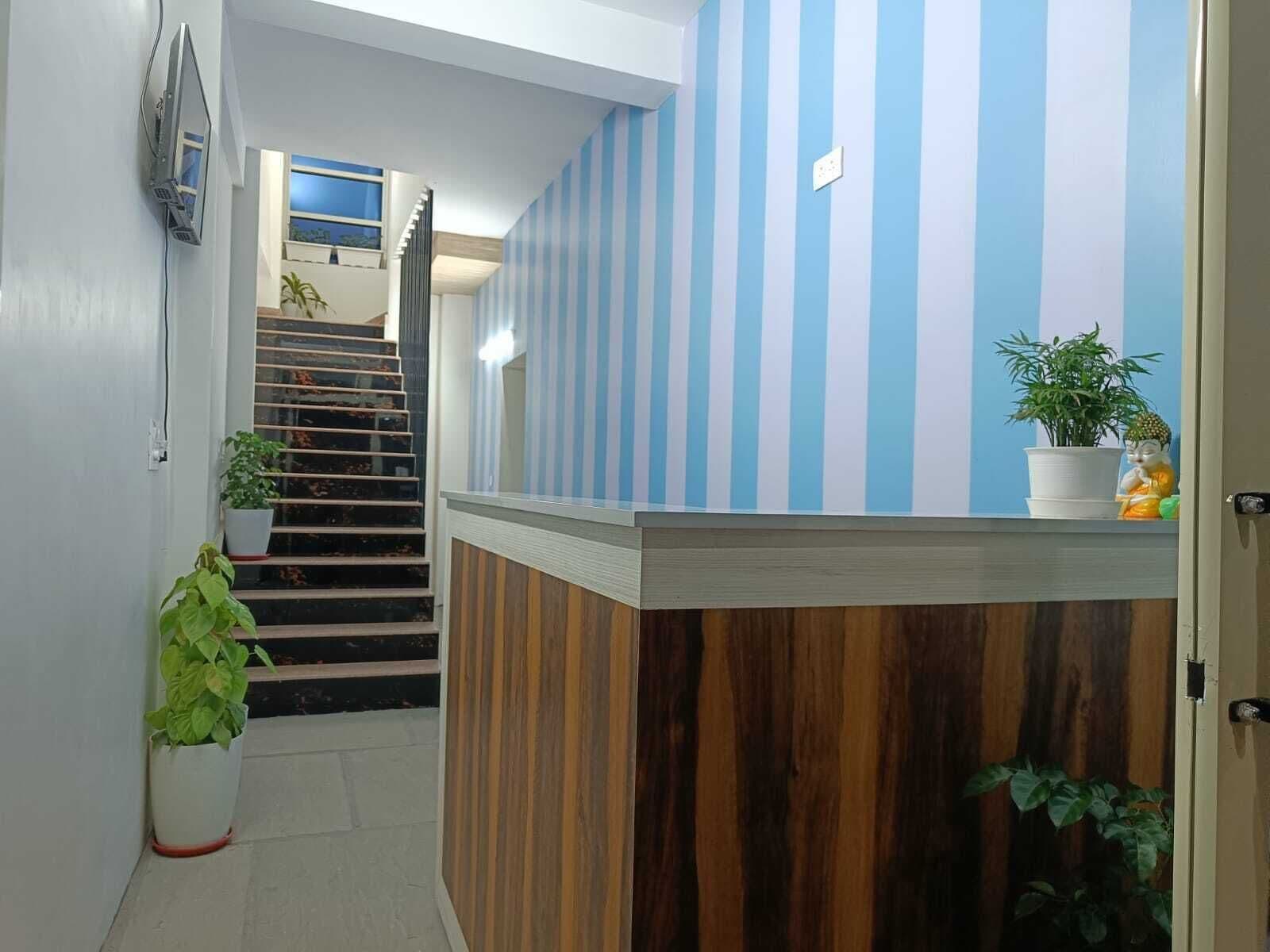Un área de recepción con pared a rayas, un mostrador de madera y una escalera que lleva a un piso superior.
