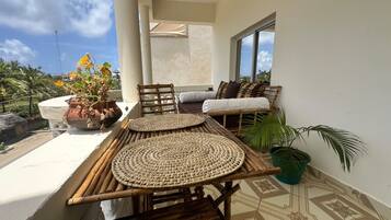 A balcony with a table and chairs, a potted plant, and a view of the sky.