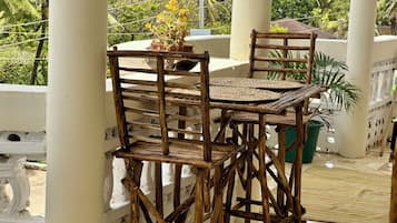 A wooden outdoor seating area with a table and chairs, surrounded by white pillars and potted plants.