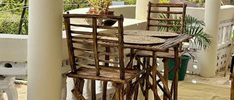 A wooden outdoor seating area with a table and chairs, surrounded by white pillars and potted plants.